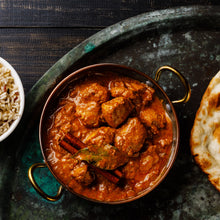 Load image into Gallery viewer, Image of a metal dish of chicken curry on a ceramic surface with a partial view of a naan bread
