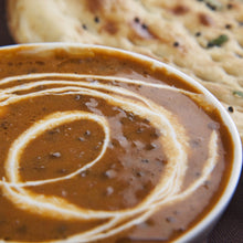 Load image into Gallery viewer, Image of a Urad Dal/Dal Makhni with a swirl of cream on the top. With a partial view of a naan bread
