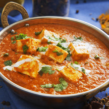 Load image into Gallery viewer, Image of a metal bowl containing paneer curry sitting on a blue table cloth. With some spices in the surrounding view
